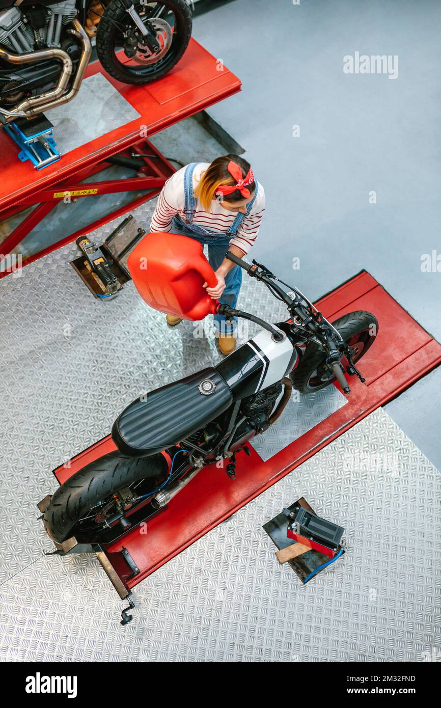 Donna meccanica con jerry può riempire serbatoio carburante di moto in fabbrica Foto Stock