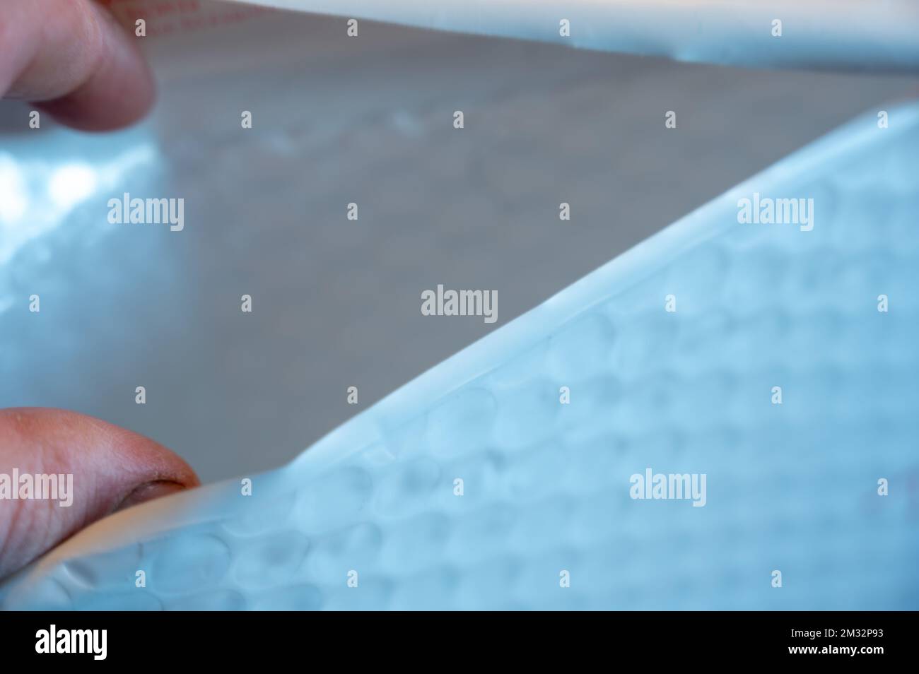 Mano caucasica che apre una busta imbottita bianca. Foto Stock