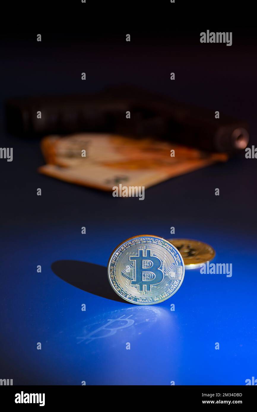 Bitcoin moneta in primo piano con una pistola e euro, defocused in background, nel buio. Fotografia e luci da studio Foto Stock
