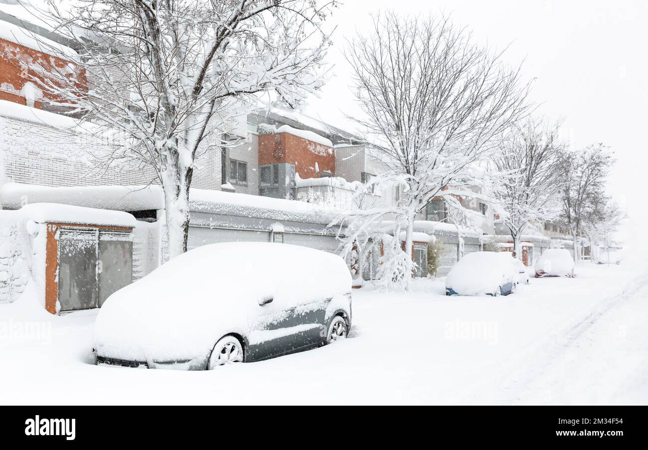 Strada residenziale completamente innevata con auto coperte di neve parcheggiate all'ingresso delle case. Paesaggio invernale. Spazio per il testo. Foto Stock