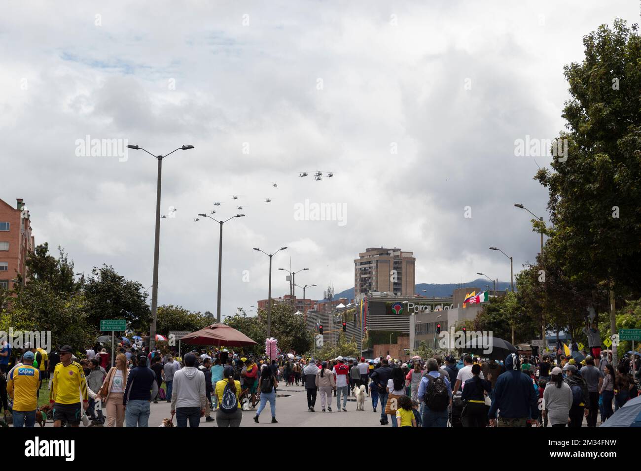 La gente cammina nel mezzo del viale Boyaca con un elicottero militare Black Hawk sullo sfondo durante la parata delle forze armate del giorno dell'indipendenza colombiana. Foto Stock