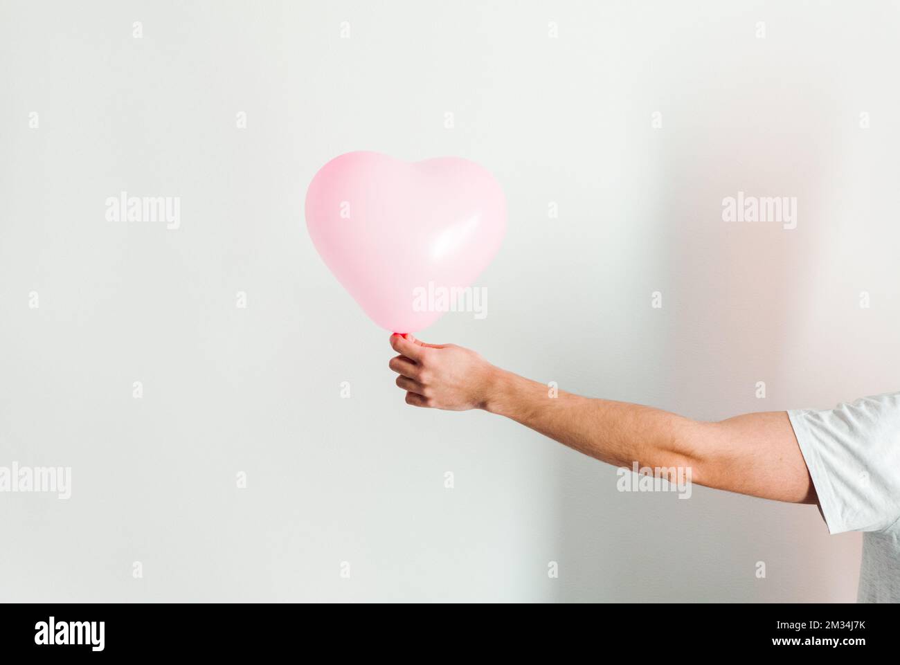 Palloncino gonfiabile a forma di cuore rosa in mano. Sfondo bianco. Foto Stock