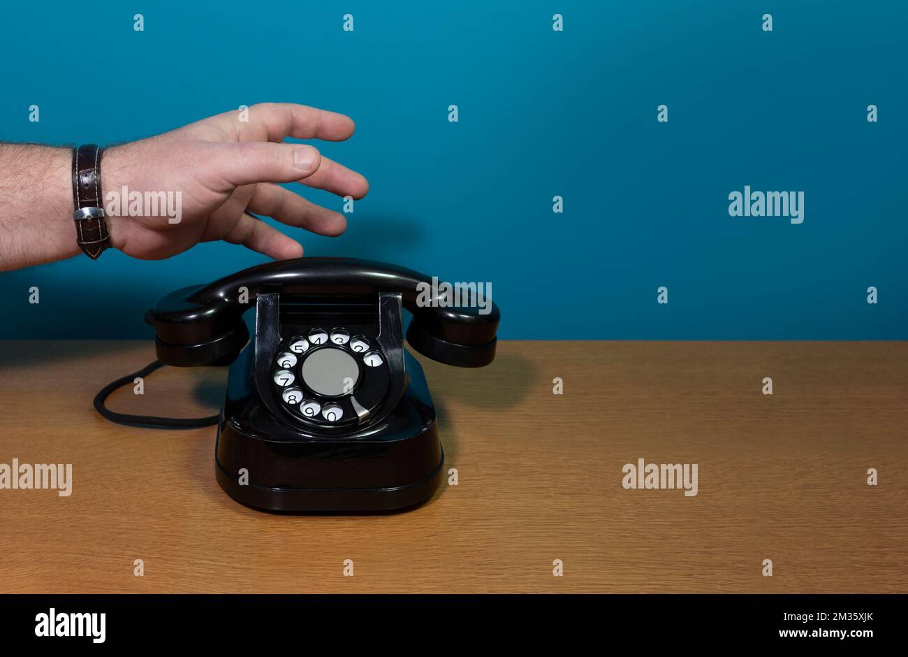 La mano raggiunge il telefono. Vecchio apparecchio telefonico su un tavolo di legno, installazione retrò. Spazio di copia Foto Stock