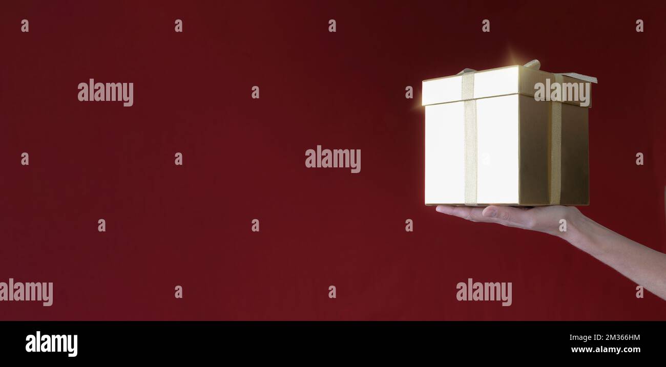Una mano donna tiene una scatola regalo su uno sfondo rosso-bordeaux. copia banner spazio Foto Stock