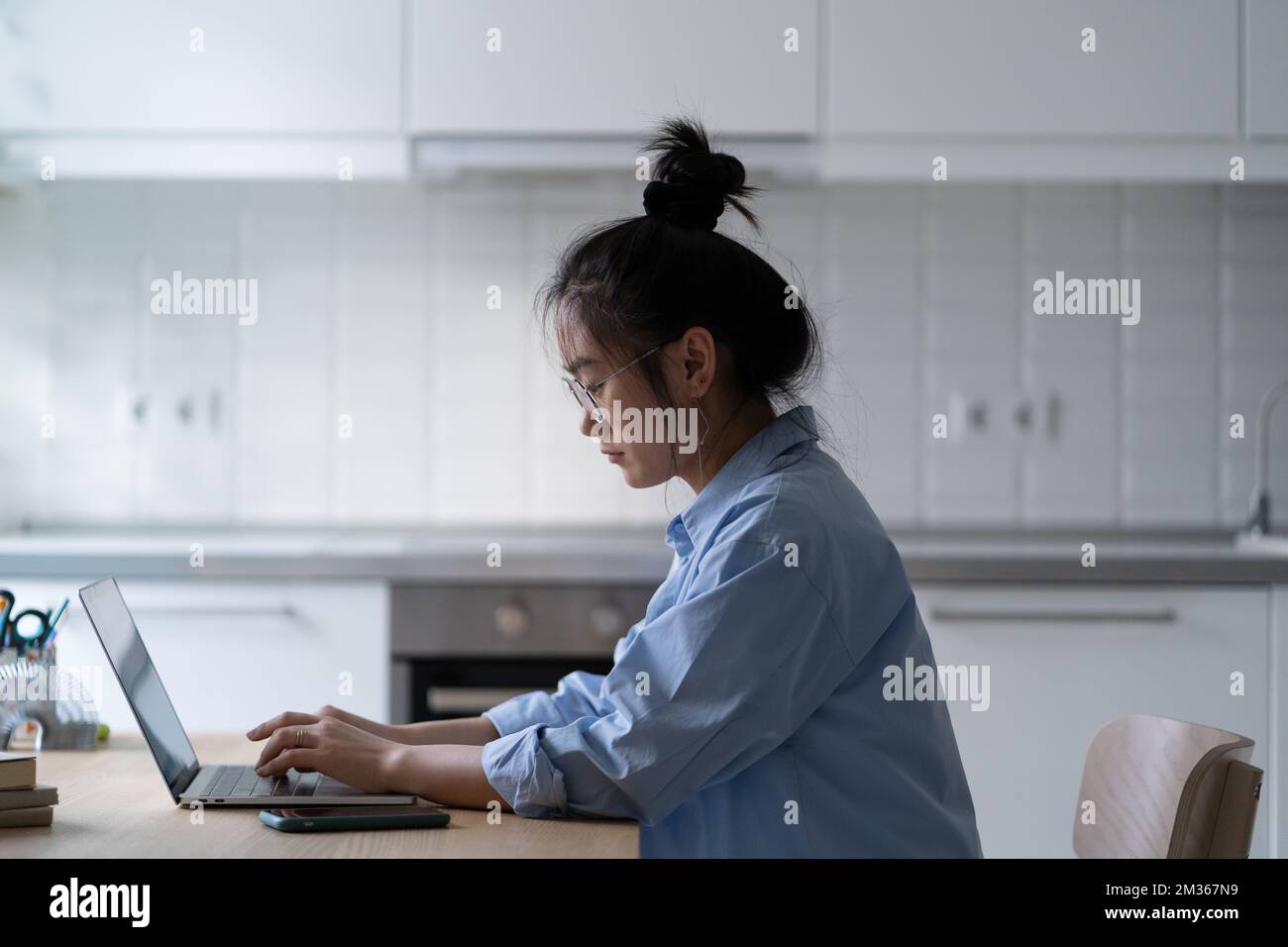Focalizzato giovane asiatica freelance blogger lavorare su laptop in cucina Foto Stock