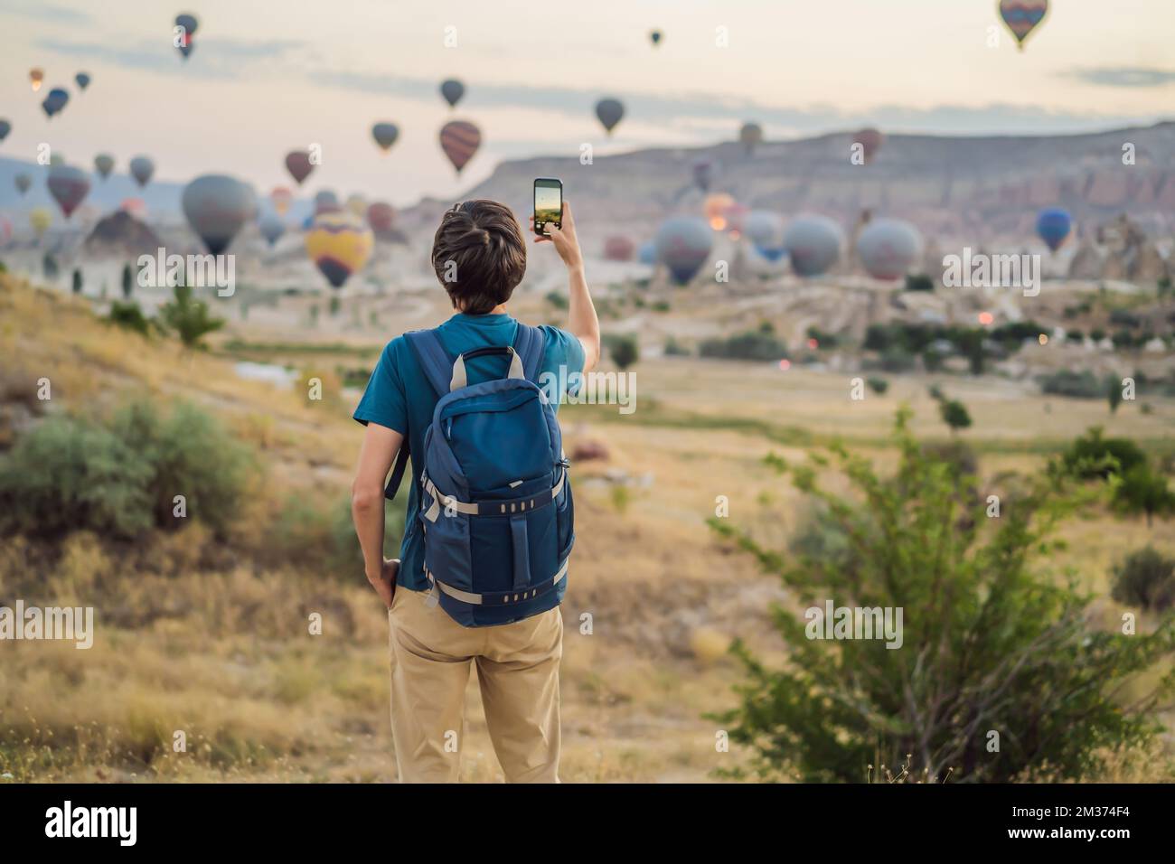 Turista che guarda mongolfiere in Cappadocia, Turchia. Buon viaggio in Turchia concetto. Uomo sulla cima di una montagna godendo di una vista meravigliosa Foto Stock