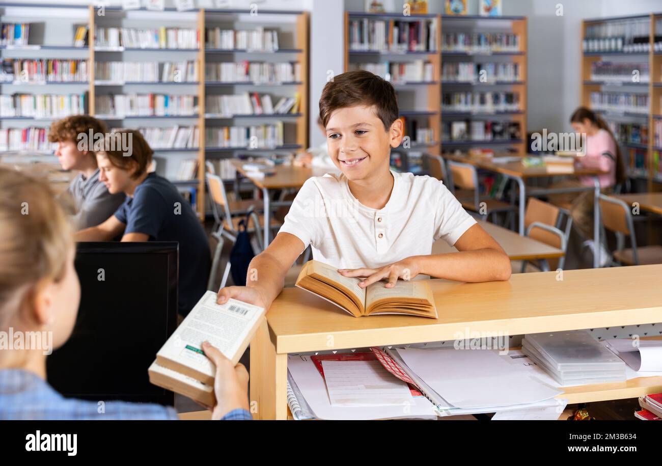 Il ragazzo dà i libri letti al bibliotecario della biblioteca scolastica Foto Stock