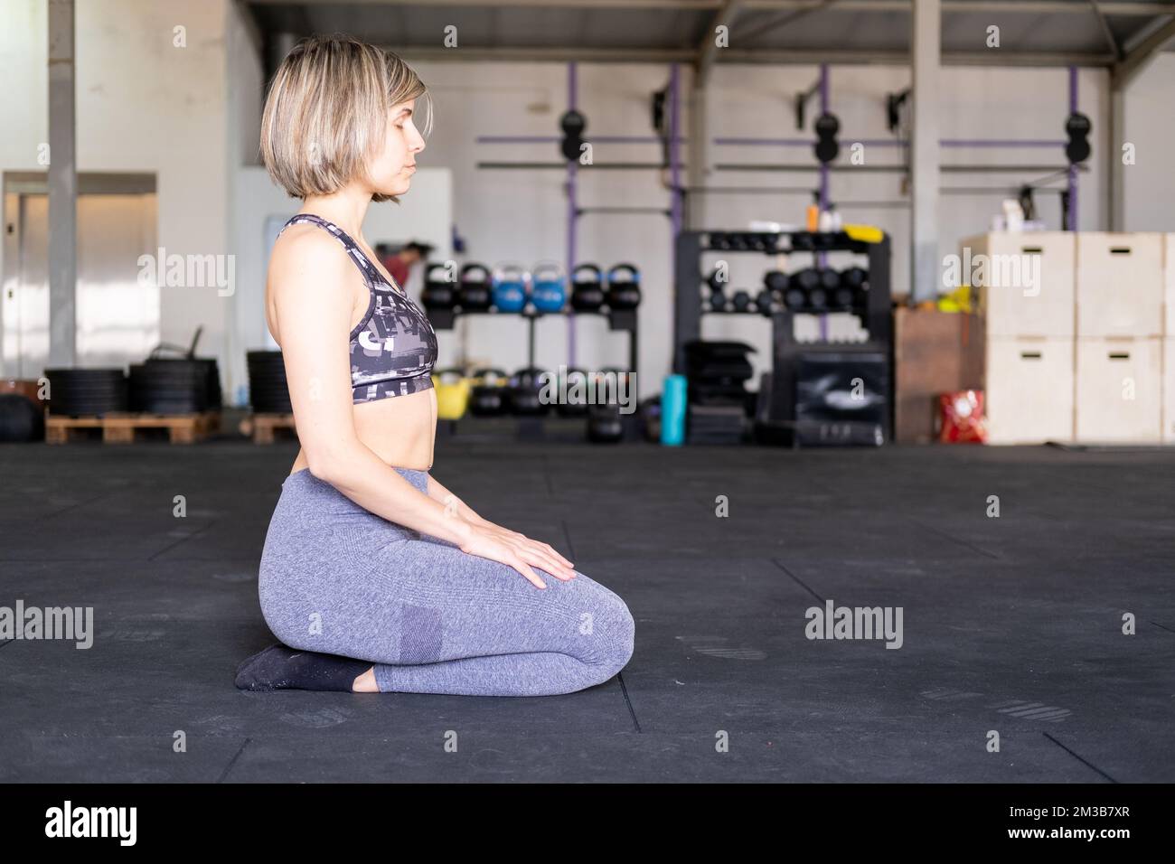 Una donna bionda media adulta meditando in ginocchio o vajrasana posa con gli occhi chiusi durante il suo flusso di vinyasa yoga pratica da solo e indossando leggings e. Foto Stock