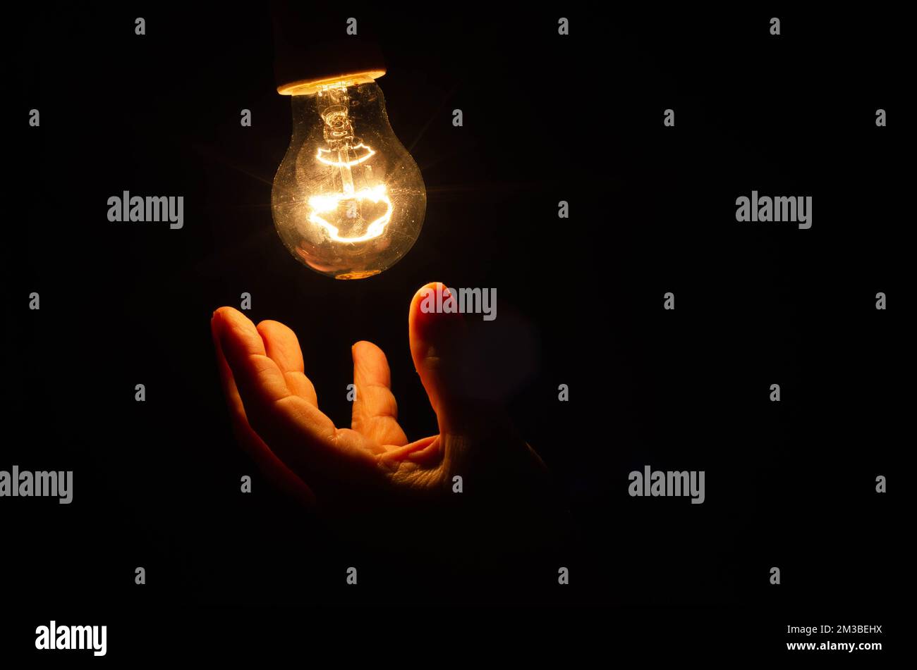 Concetto di consumo di elettricità, in questi tempi di crisi, rappresentato da una lampadina e monete in euro sparse, sfondo scuro Foto Stock