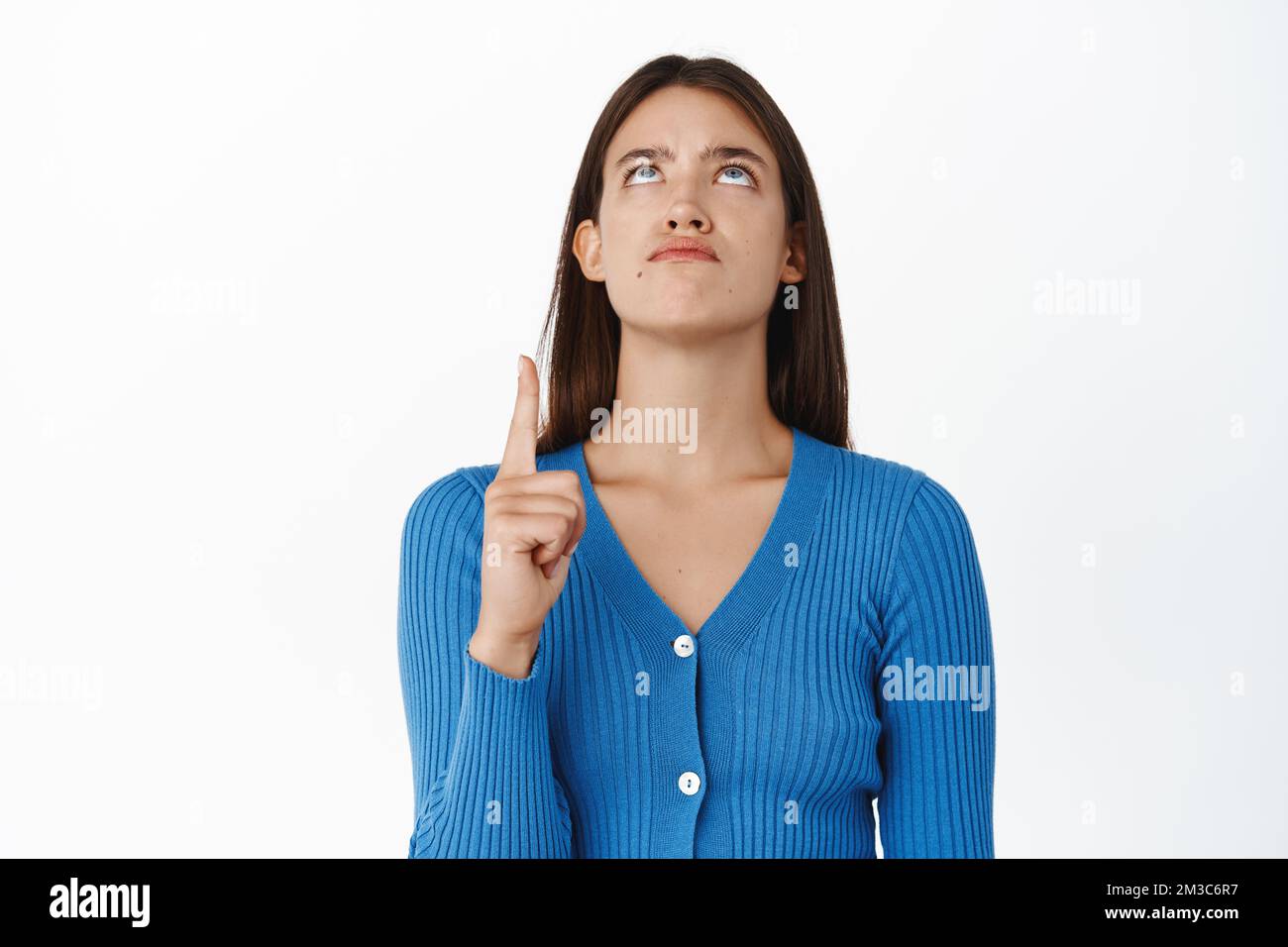 Donna dispiaciuto brunetta che si alza, puntando il dito con fastidioso grumpy espressione del viso, indossando blusa blu, sfondo bianco Foto Stock