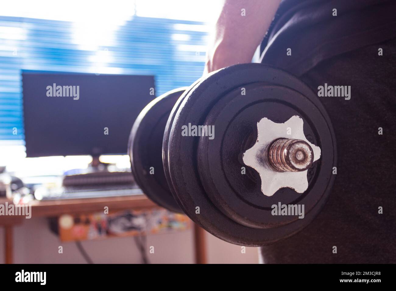 Primo piano con un giovane che tiene e stringe un mumbbel di ferro con sfondo della stanza. Ideale per il fitness, lo sport, l'allenamento domestico, l'allenamento al coperto e il benessere Foto Stock