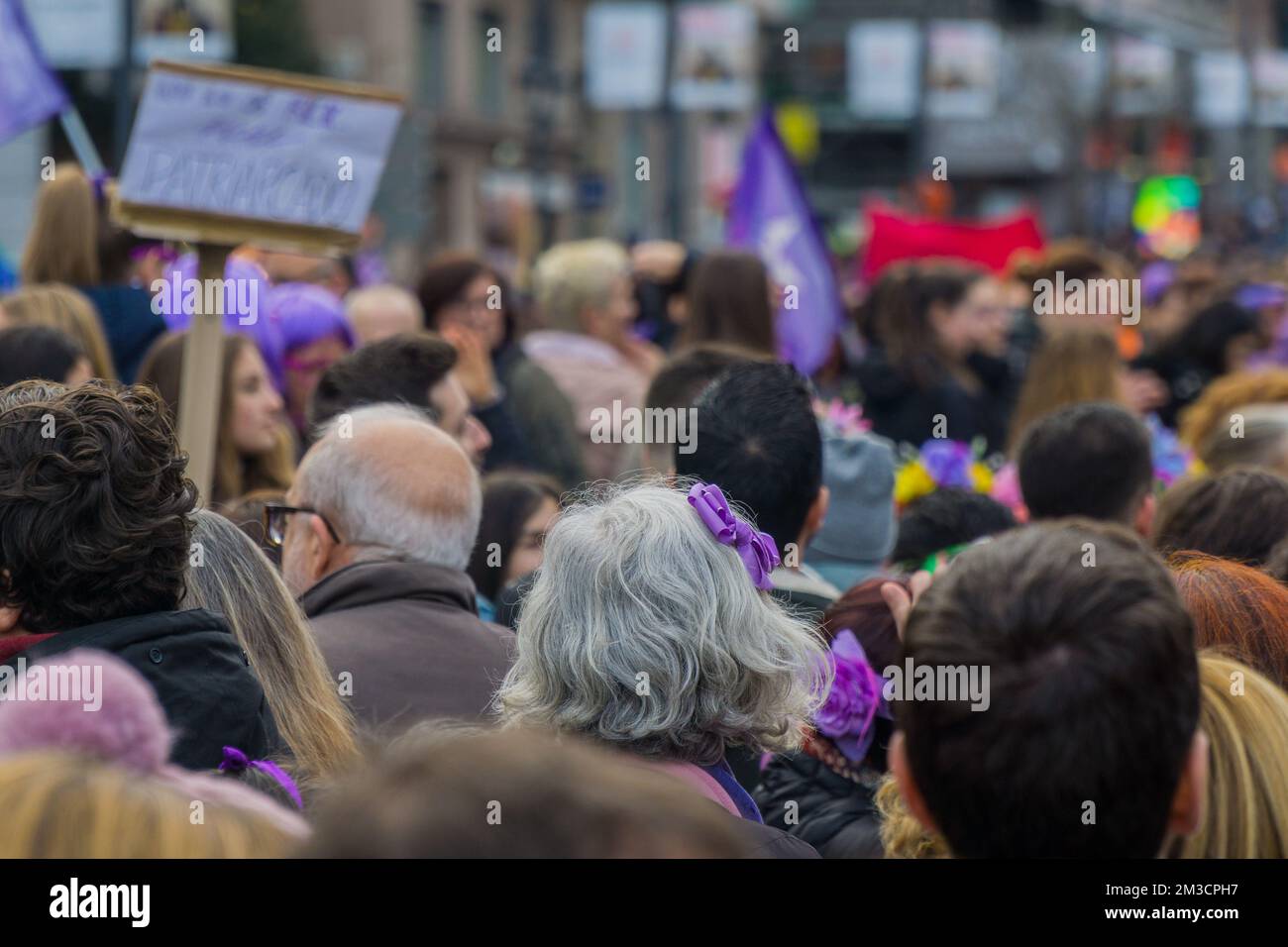 Closeup ad una vecchia donna con capelli grigi e nastro viola mordente in mezzo ad una folla durante 8M marce nella Giornata Internazionale della Donna, affermando la sua r Foto Stock