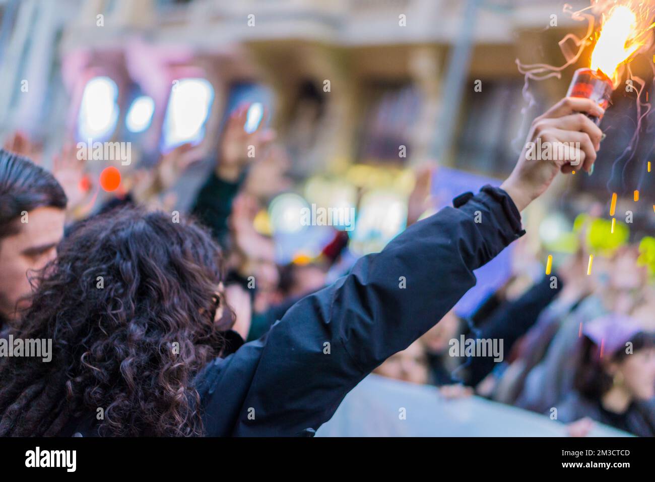 Closeup ad una donna riccia capelli neri che tiene un bagliore di fumo rosso nel mezzo di una folla durante 8M marce nel giorno internazionale delle donne, sostenendo lei Foto Stock