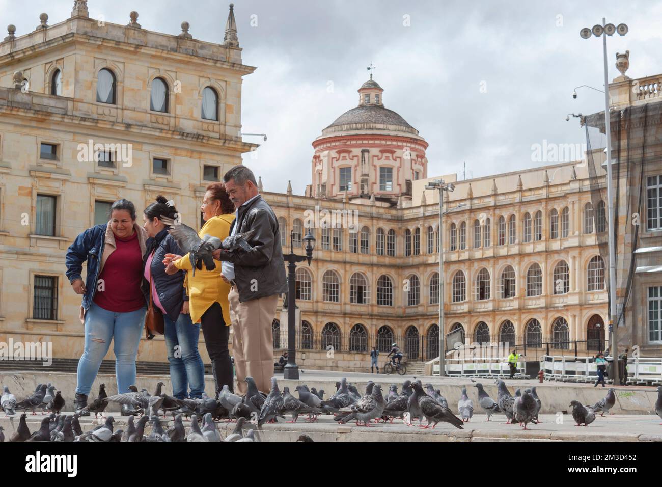 Una Famiglia Turistica che alimenta i piccioni in posa per una foto in mezzo a piazza bolivar con san bartolome scuola superiore sullo sfondo in centro Foto Stock