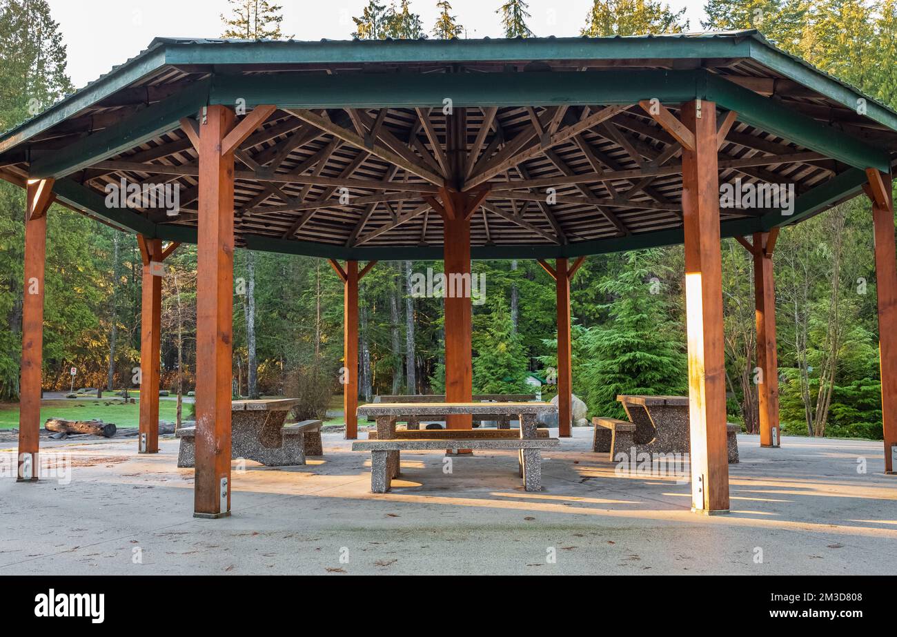 Pergola in legno nel parco con tavoli da giardino e sedie all'ombra. Summerhouse in legno si trova in un parco verde mattutino. Nessuno, fuoco selettivo Foto Stock