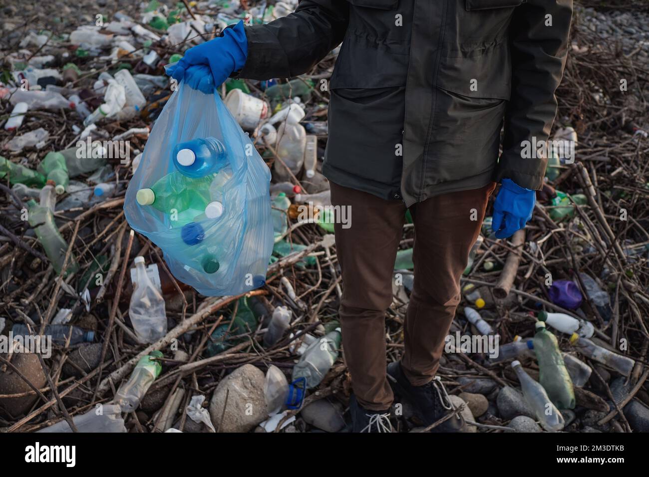 Processo di pulizia della spiaggia di pietra dai rifiuti di plastica. L'uomo tiene bottiglie di plastica nel sacchetto dei rifiuti. Concetto di inquinamento ambientale. Foto Stock