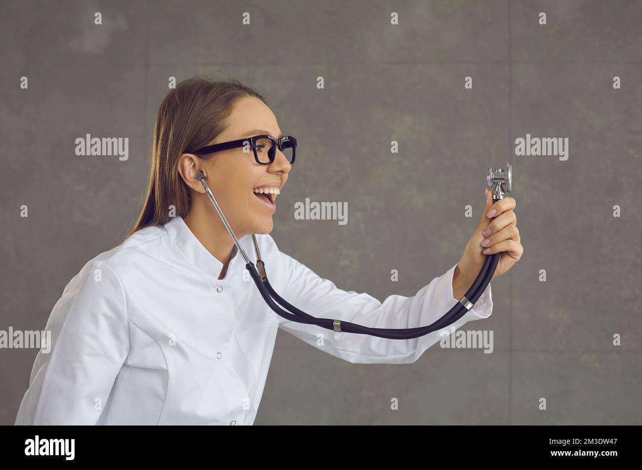 Vista del profilo di una giovane donna sorridente medico o infermiera che tiene fuori uno stetoscopio e l'ascolto. Foto Stock