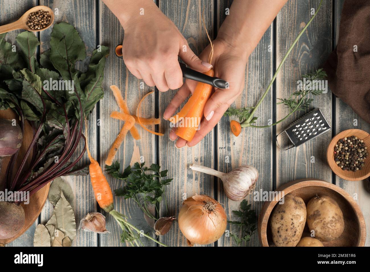 Donna irriconoscibile che sbuccia la carota con coltello nero vicino a  ciotola di legno marrone con patate, ciotola piccola con pepe, grattugia  piccola, cipolla, aglio, b Foto stock - Alamy
