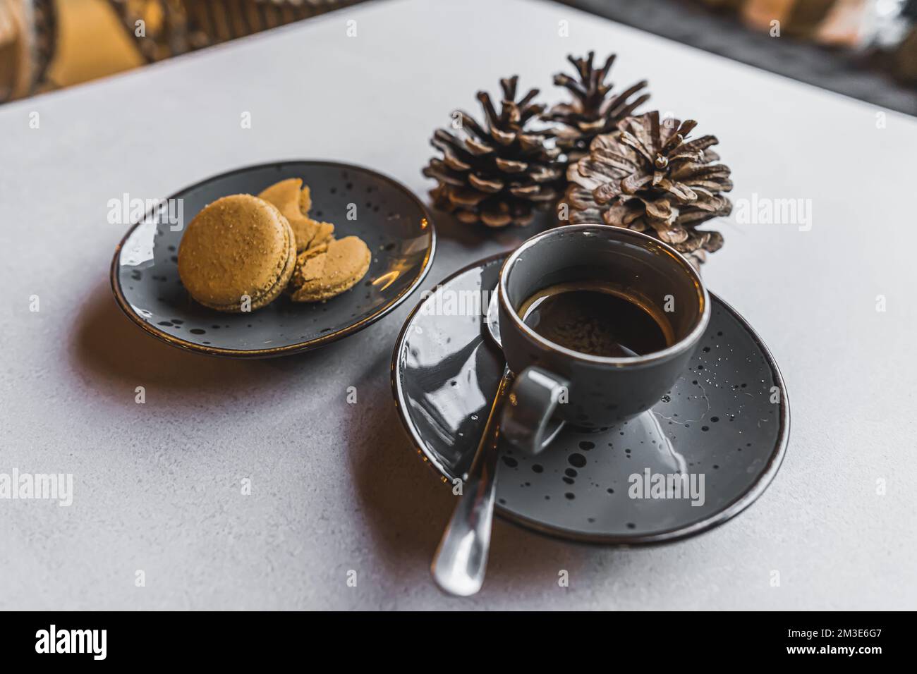 Macaron dorati serviti con una tazza di caffè caldo su un tavolo bianco decorato con coni di pino. Dessert festivi. Cottura di Natale. Scatto orizzontale in interni. Foto di alta qualità Foto Stock