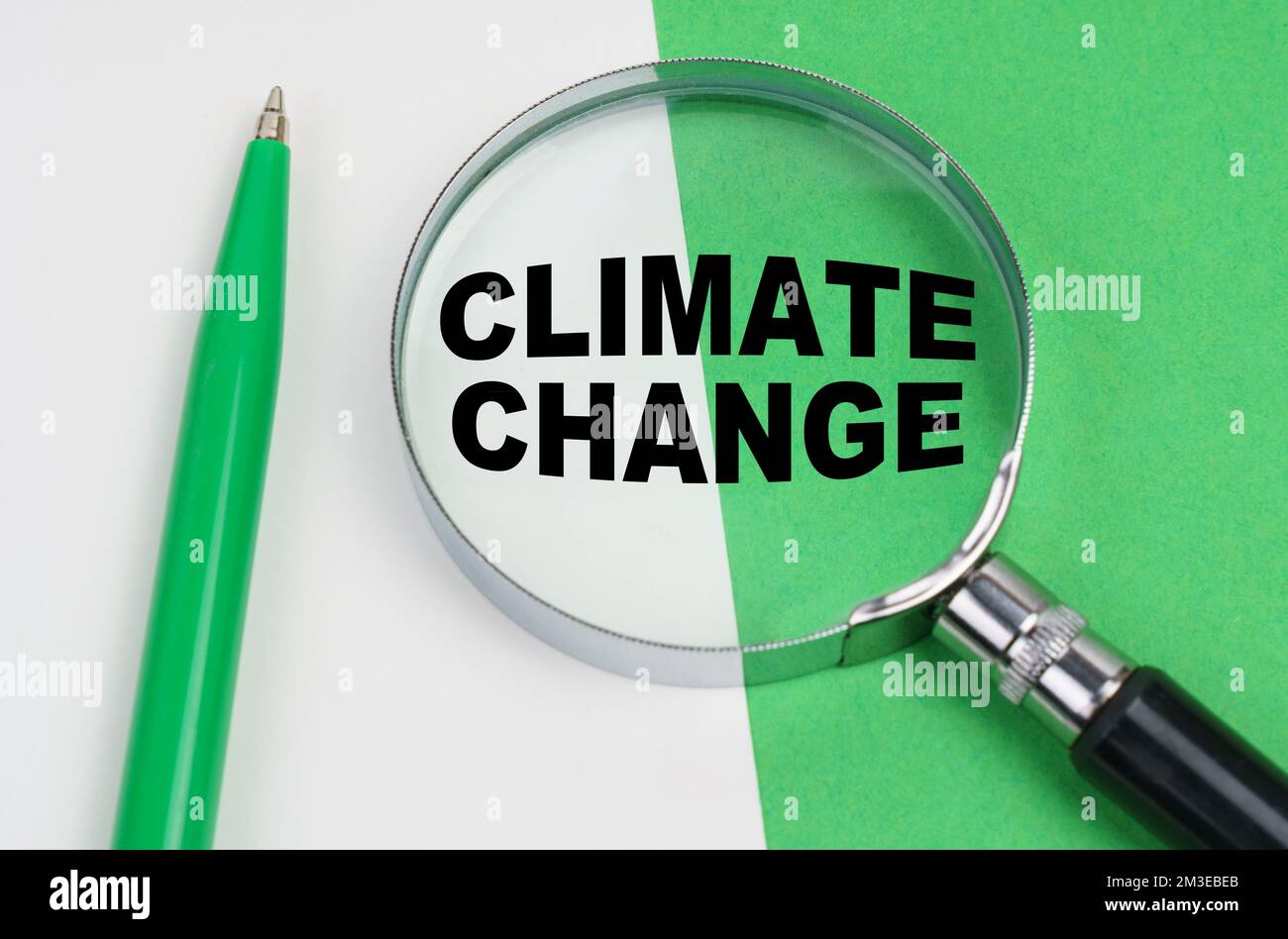 Concetto ecologico. Su uno sfondo bianco-verde si trova una penna e una lente d'ingrandimento, all'interno della quale si trova l'iscrizione - cambiamento climatico Foto Stock