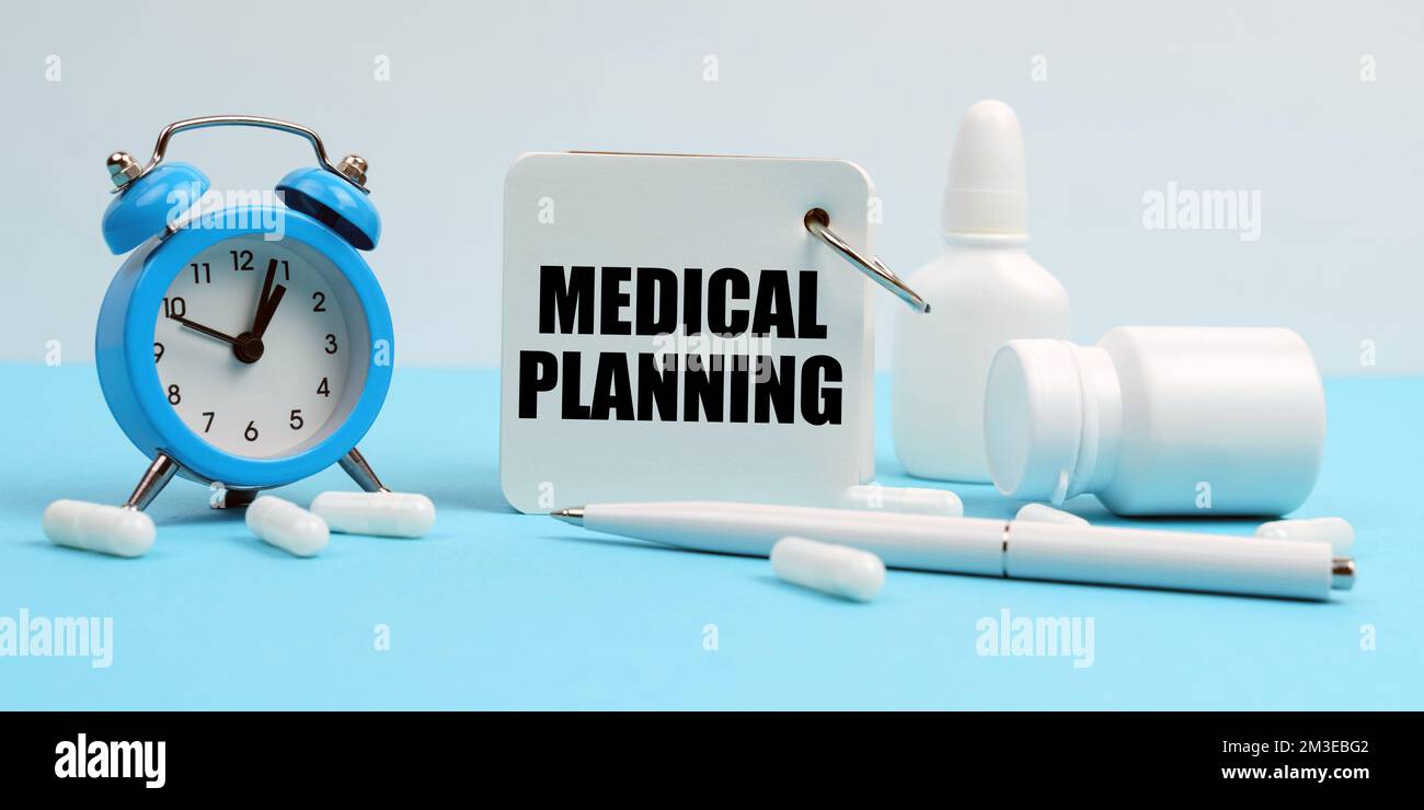 Medicina e concetto di salute. Su una superficie blu si trovano pillole, un orologio sveglia e un notebook con l'iscrizione - PIANIFICAZIONE MEDICA Foto Stock