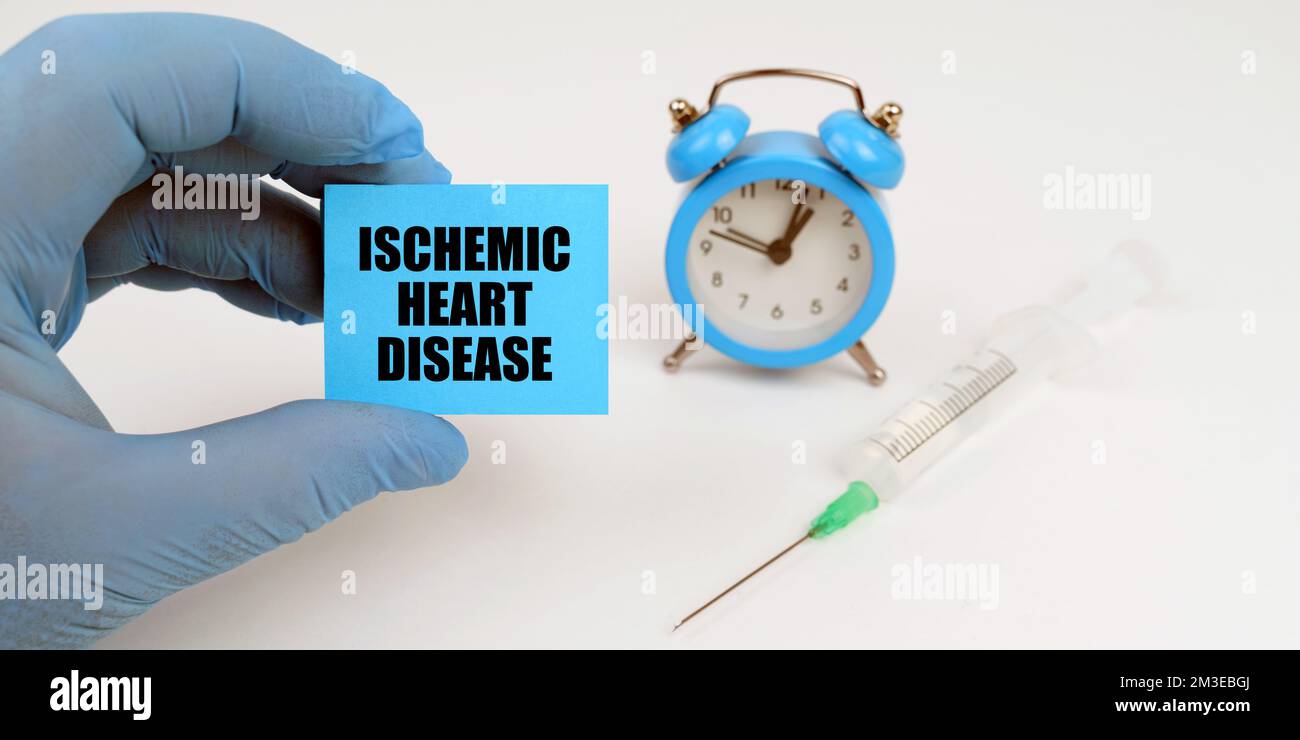 Concetto di medicina. Sul tavolo c'è una siringa e una sveglia, in mano un notebook con l'iscrizione - cardiopatia ischemica Foto Stock