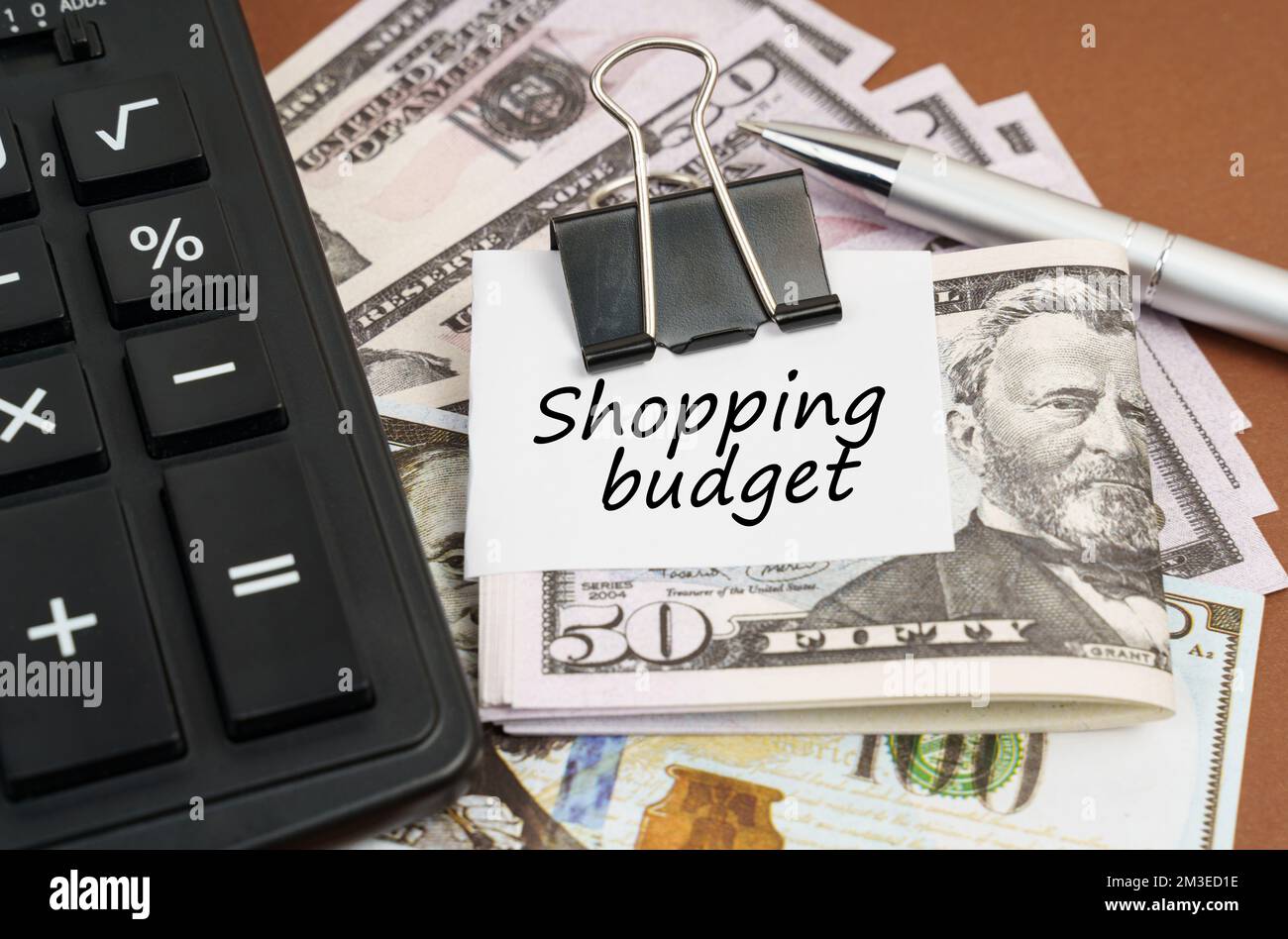 Concetto finanziario e commerciale. Su uno sfondo marrone si trova una calcolatrice e dollari su una clip con un'iscrizione su carta - bilancio dello Shopping Foto Stock