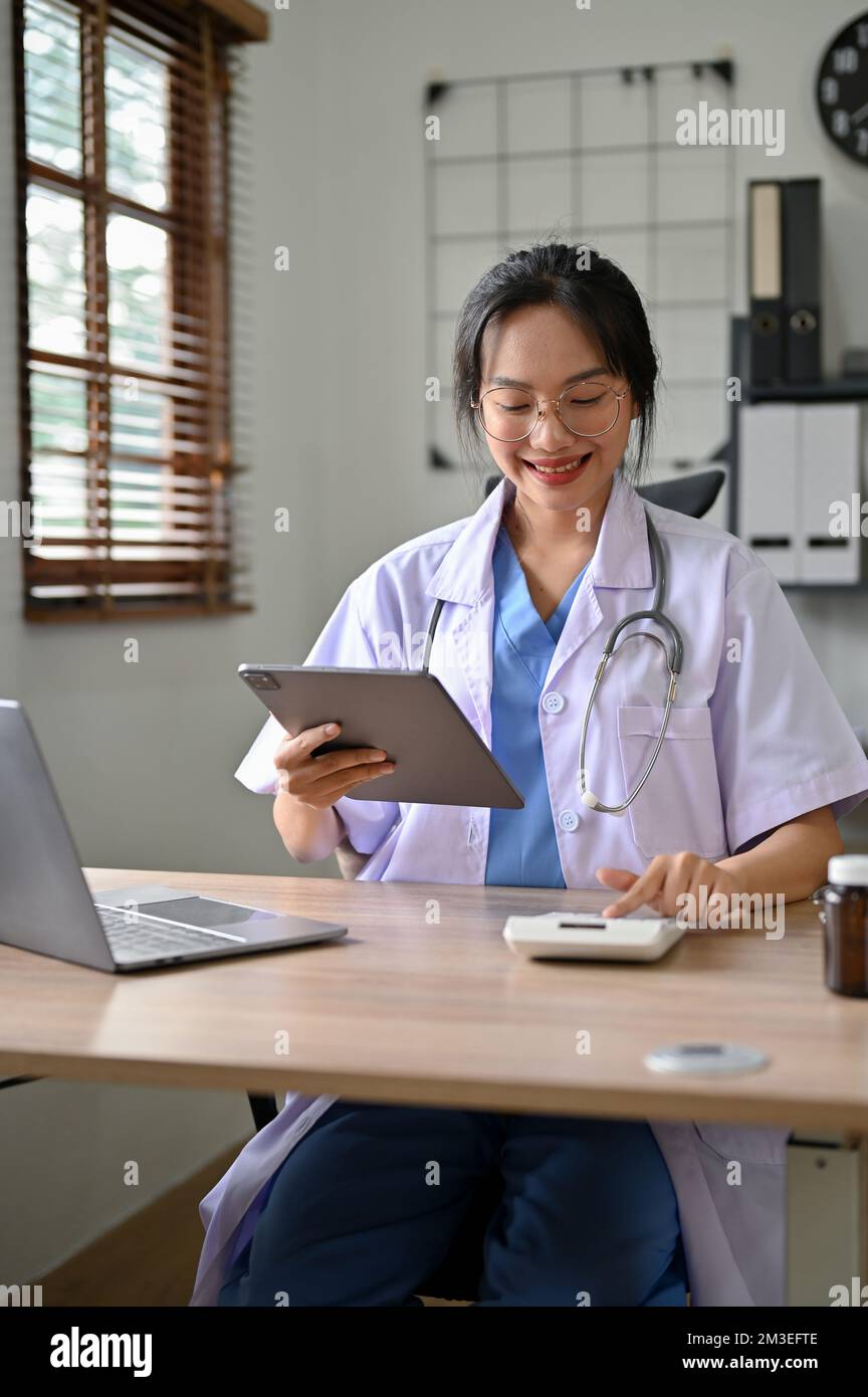 Ritratto, bella medico asiatico utilizzando calcolatrice, stimare il costo della chirurgia per la sua paziente, lavorando in ufficio. Foto Stock