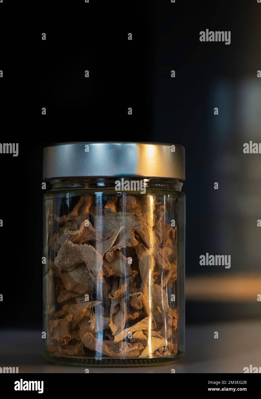 fettine di zenzero essiccate in un vasetto di vetro con coperchio metallico. Condimento esotico per cibi e bevande. Fotografia di cibo scuro Foto Stock