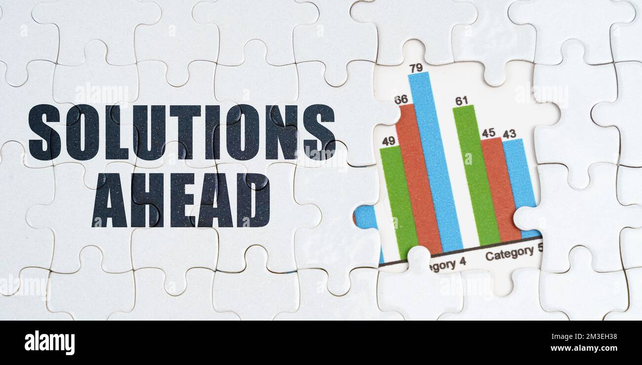 Economia e business concept. Sui puzzle bianchi c'è un'iscrizione - soluzioni avanti. Grafico finanziario nella finestra tra i puzzle Foto Stock
