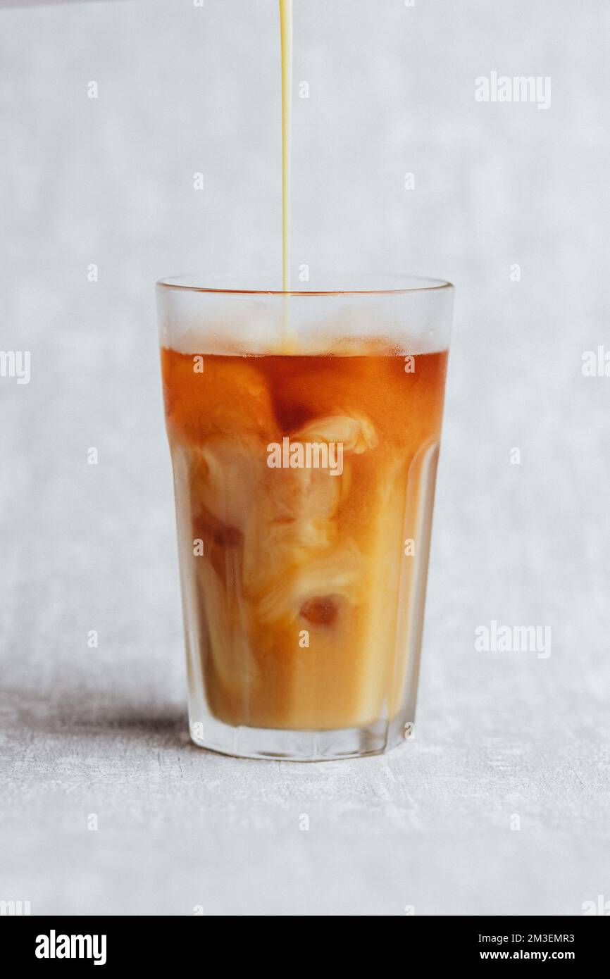 Una verticale di versare latte di soia alla vaniglia in una bevanda di caffè speciale con ghiaccio Foto Stock