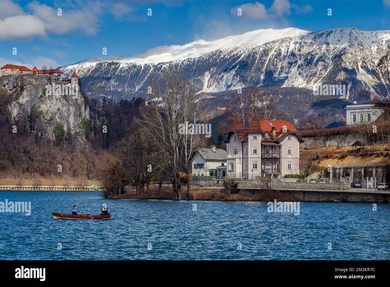 Bled, Slovenia - Lago di Bled con una piccola barca e il Castello di Bled e le Alpi Giulie sullo sfondo in una giornata invernale di sole Foto Stock