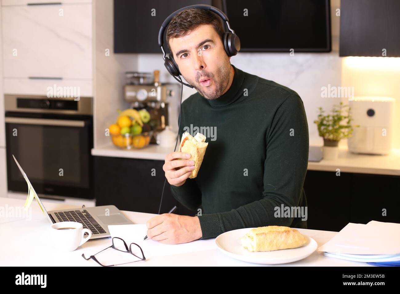 Uomo impegnato a mangiare un panino durante una chiamata in conferenza Foto Stock