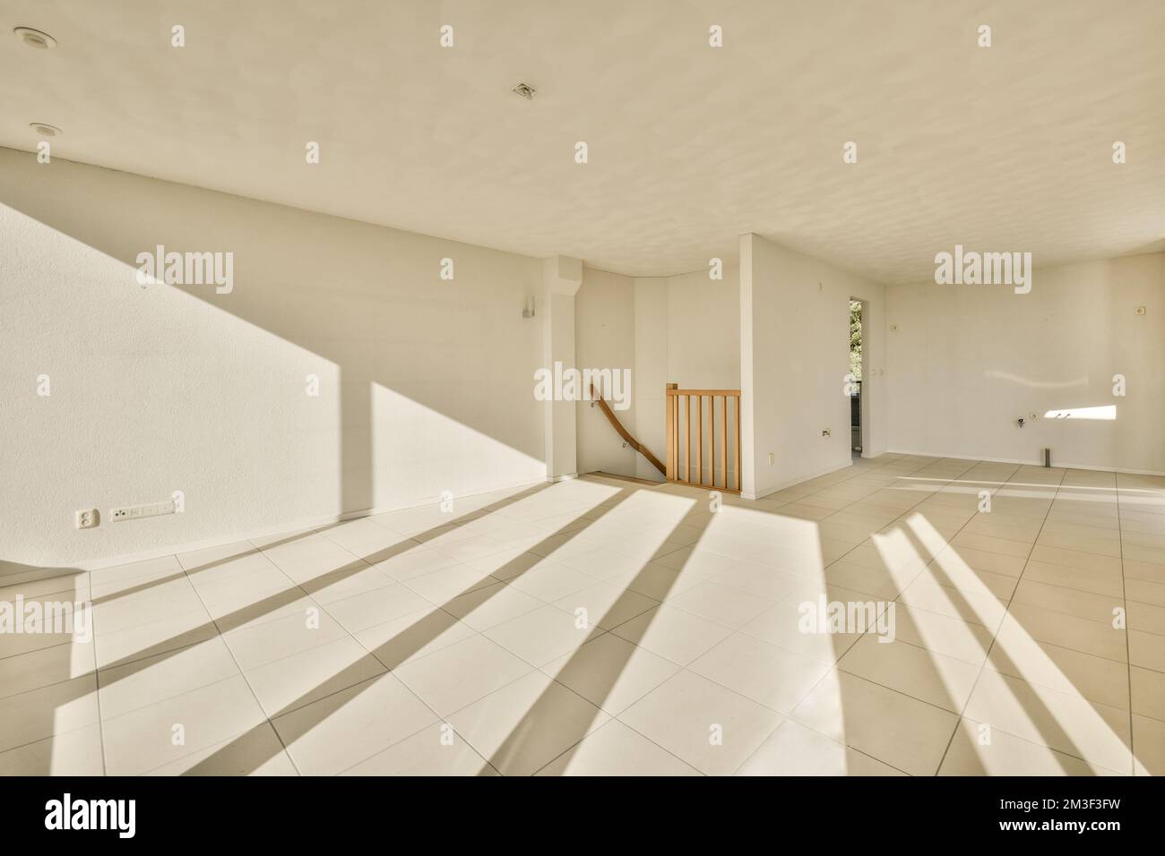 un soggiorno vuoto con pavimento in piastrelle bianche e scala in legno che conduce al secondo piano di questa casa Foto Stock