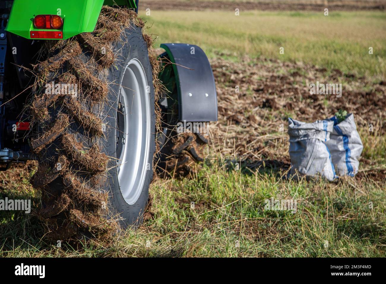 Concetto di agricoltura. Ruota del trattore ricoperta di fango, sacco con semi, sfocatura sfondo incolto dell'azienda agricola. Inizio stagione agricola. Foto Stock