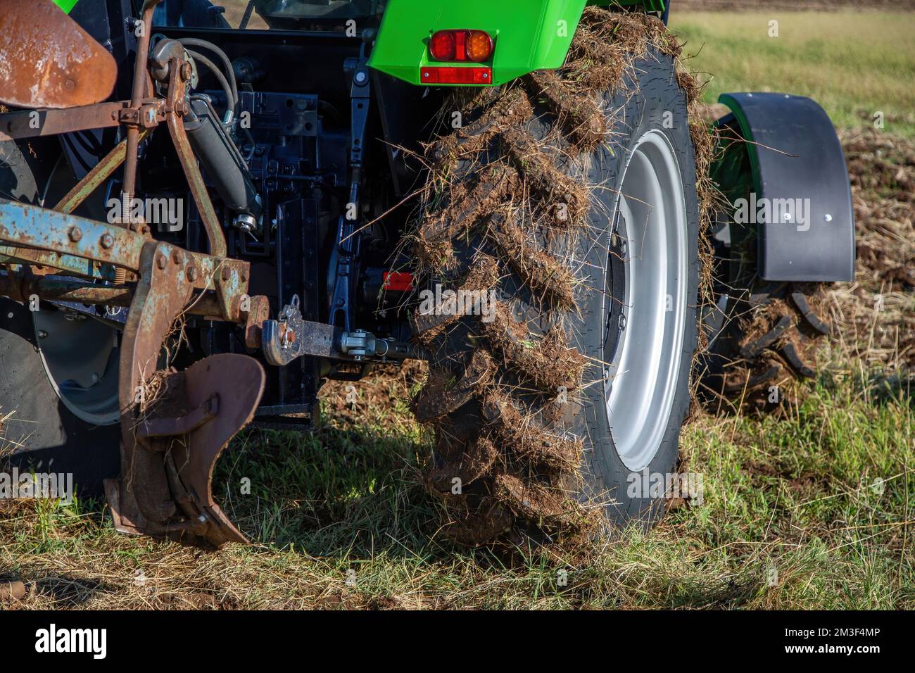 Concetto di agricoltura. Trattore con aratro, vista ravvicinata della ruota ricoperta di fango, fondo agricolo non coltivato. La stagione agricola è iniziata. Foto Stock