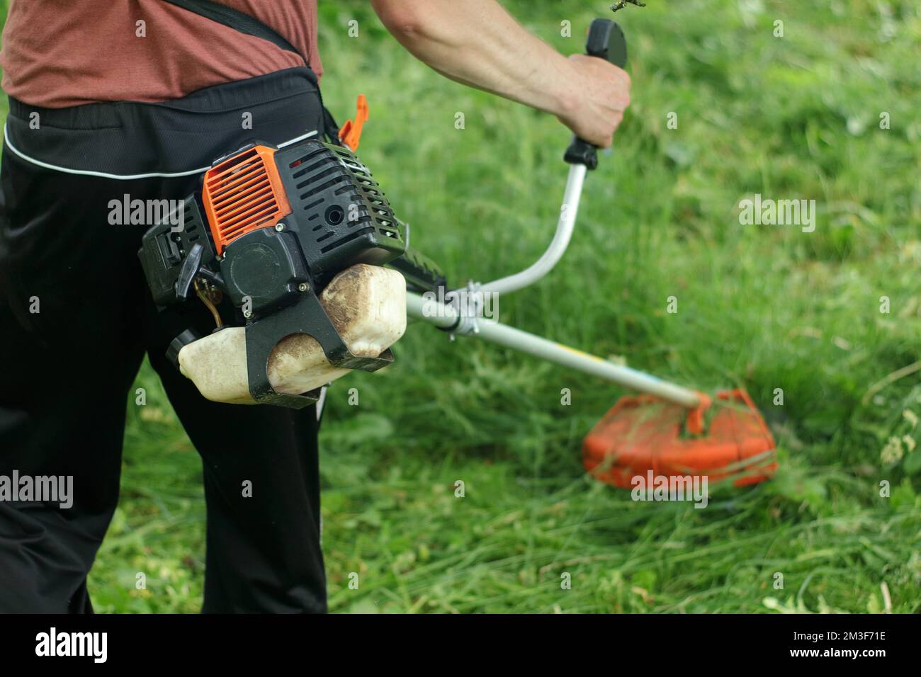 Lavoratore che taglia l'erba con un tagliaerba a benzina nel parco  cittadino o nel cortile.