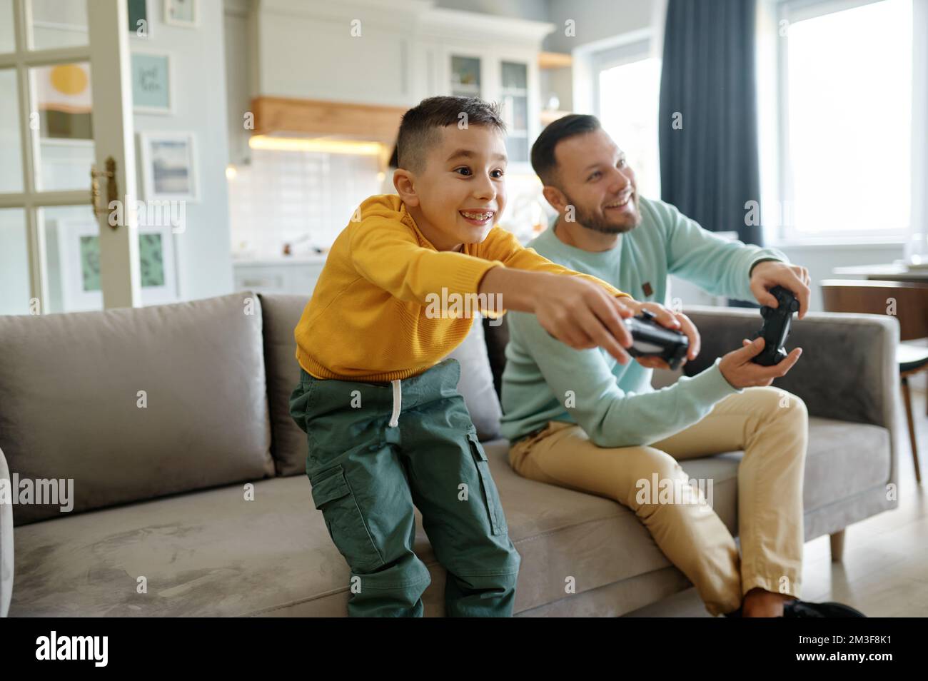 Papà e figlio che giocano a videogiochi mentre la mamma cucinava in cucina Foto Stock