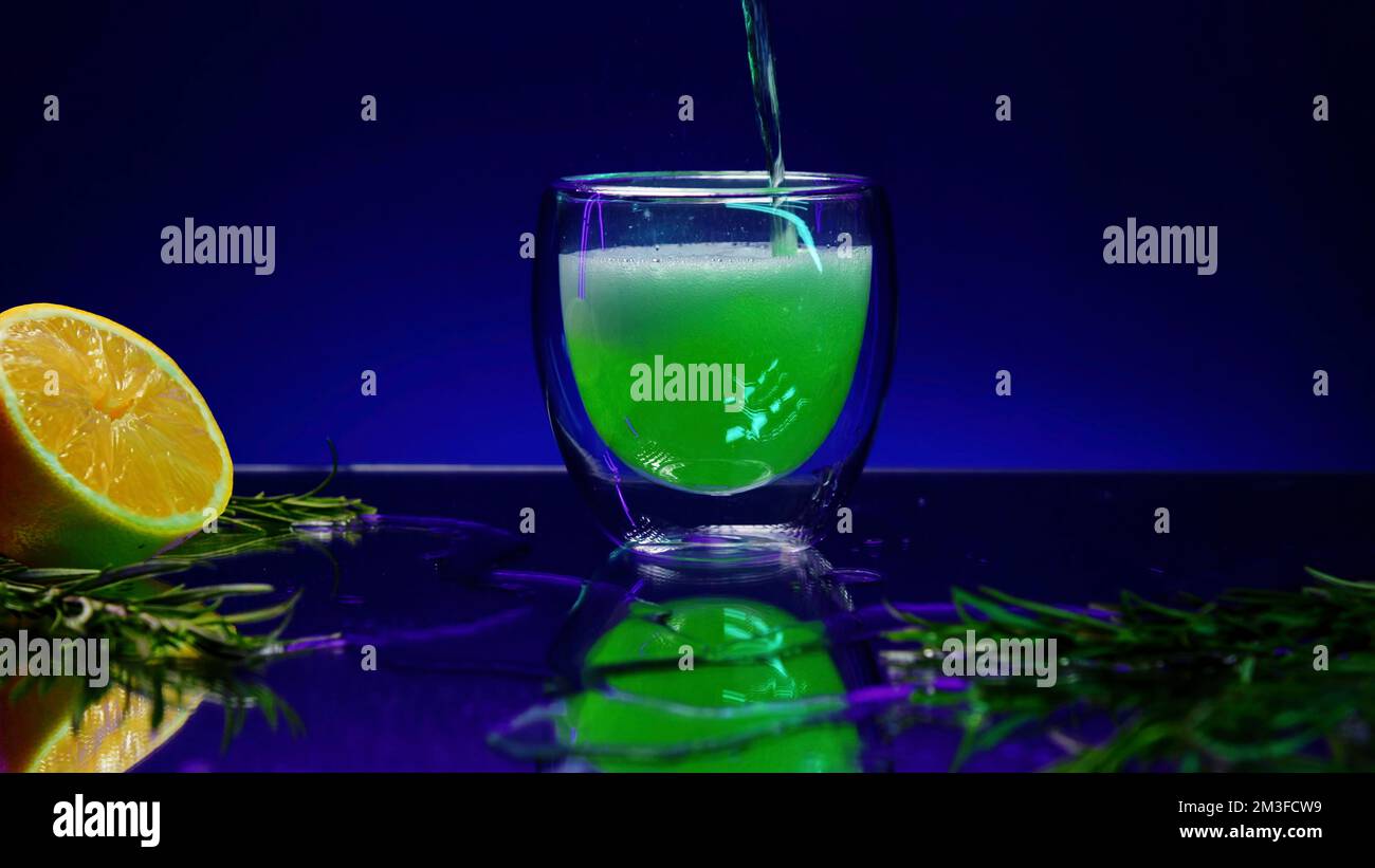 Primo piano di una bevanda da cocktail verde in un bicchiere trasparente posto sul bancone del bar. Clip di scorta. Banco bar decorato con foglie verdi e oran Foto Stock