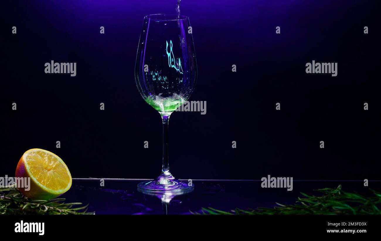 Primo piano di una bevanda da cocktail verde in un bicchiere trasparente posto sul bancone del bar. Clip di scorta. Banco bar decorato con foglie verdi e oran Foto Stock