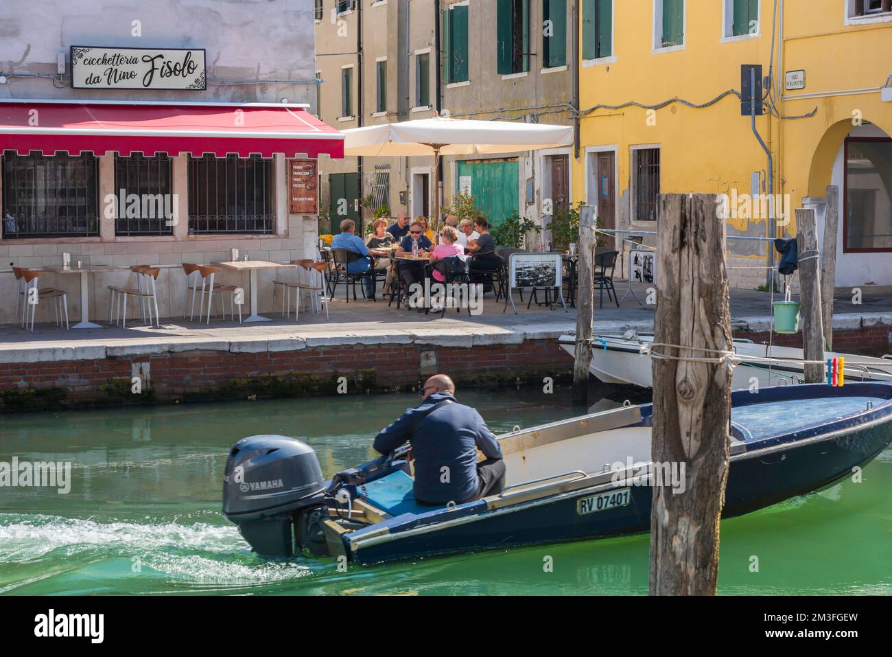 Ristorante canale Italia, vista in estate di un gruppo di persone che cenano in una terrazza ristorante accanto al canale vena a Chioggia, comune di Venezia, Italia Foto Stock