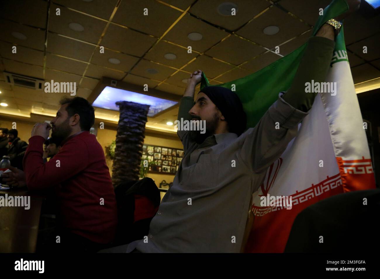 Teheran, Teheran, Iran. 14th Dec, 2022. Un fan iraniano che detiene una bandiera iraniana (R) mentre frequenta il caffè Nakhlestan nel centro di Teheran, Iran, per guardare la Coppa del mondo FIFA Qatar 2022 partita semifinale tra Francia e Marocco sullo schermo, 14 dicembre 2022. Tifosi provenienti da Iran, Libano, Yemen, Siria e Palestina si riuniscono al caffè Nakhlestan, gestito e di proprietà dell'Owj, Islamic Revolutionary Guard Corps (IRGS) Arts and Media Organization, per sostenere la nazionale marocchina. Dopo la vittoria contro il Portogallo in Qatar il 10th dicembre, i marocchini portavano bandiere palestinesi per mostrare t Foto Stock