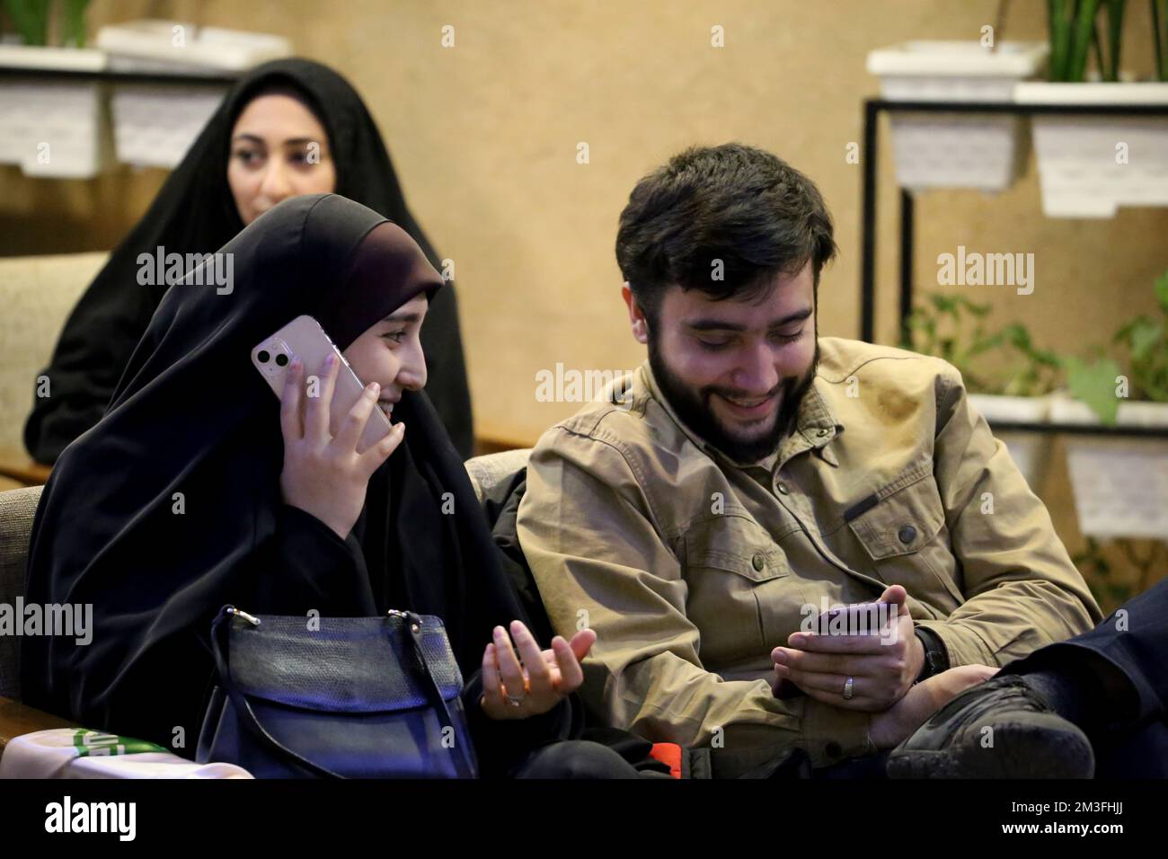 Teheran, Teheran, Iran. 14th Dec, 2022. Una coppia iraniana guarda una trasmissione dal vivo della partita semifinale di calcio della Coppa del mondo del Qatar 2022 tra Marocco e Francia al caffè Nakhlestan nel centro di Teheran, Iran, il 14 dicembre 2022. Tifosi provenienti da Iran, Libano, Yemen, Siria e Palestina si riuniscono al caffè Nakhlestan, gestito e di proprietà dell'Owj, Islamic Revolutionary Guard Corps (IRGS) Arts and Media Organization, per sostenere la nazionale marocchina. Dopo la vittoria contro il Portogallo in Qatar il 10th dicembre, i marocchini portarono bandiere palestinesi per dimostrare il loro sostegno ai palestinesi. Foto Stock