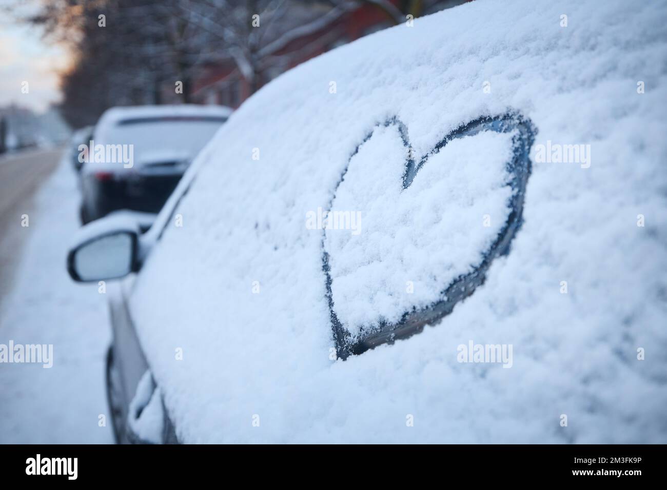 Forma del cuore come segno d'amore sul finestrino dell'auto innevato. Parcheggio su strada coperta di neve in inverno. Foto Stock