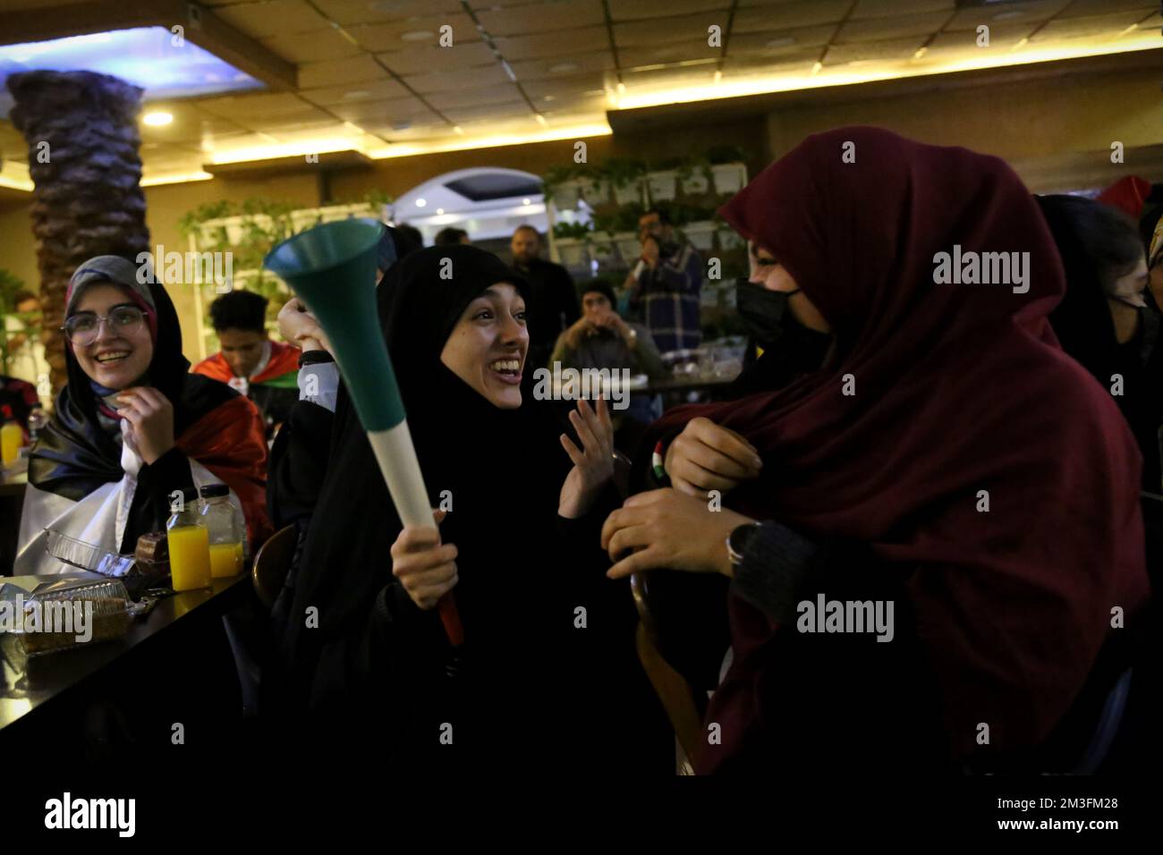 Teheran, Teheran, Iran. 15th Dec, 2022. Le velate fan iraniane reagiscono mentre uno di loro tiene un corno mentre guarda sullo schermo la semifinale della Coppa del mondo FIFA Qatar 2022 tra Francia e Marocco, al caffè Nakhlestan nel centro di Teheran, in Iran, il 15 dicembre 2022. Tifosi provenienti da Iran, Libano, Yemen, Siria e Palestina si riuniscono al caffè Nakhlestan, gestito e di proprietà dell'Owj, Islamic Revolutionary Guard Corps (IRGS) Arts and Media Organization, per sostenere la nazionale marocchina. Dopo la vittoria contro il Portogallo in Qatar il 10th dicembre, i marocchini portavano bandiere palestinesi a. Foto Stock