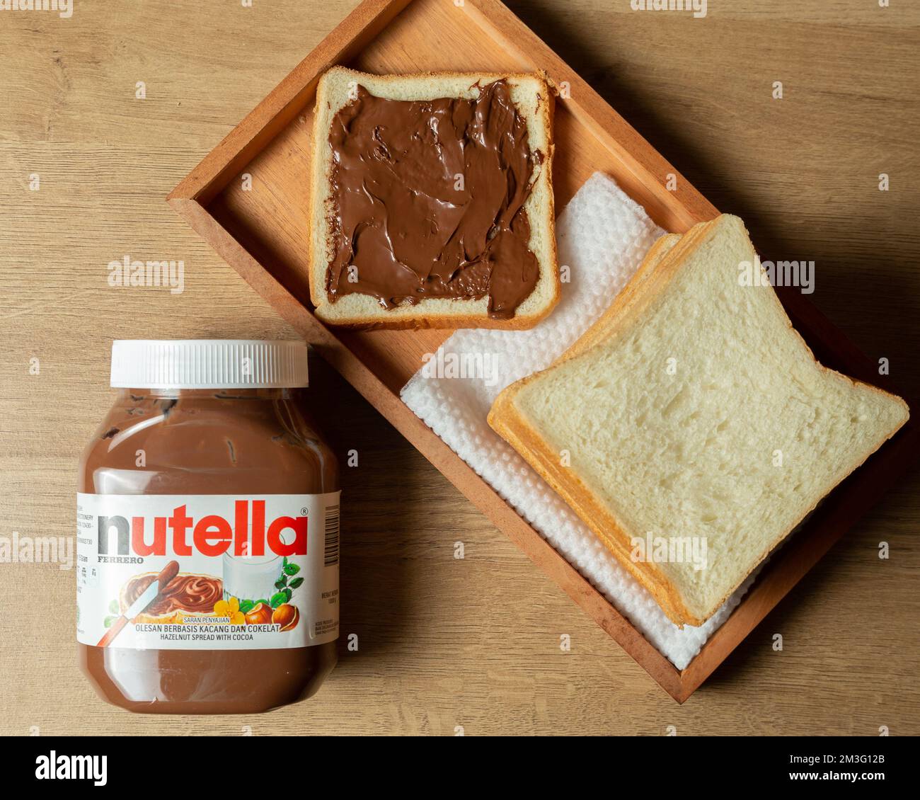 Nutella con bottiglie grandi e piccole e un po' di pane bianco ordinato sul tavolo da pranzo Foto Stock