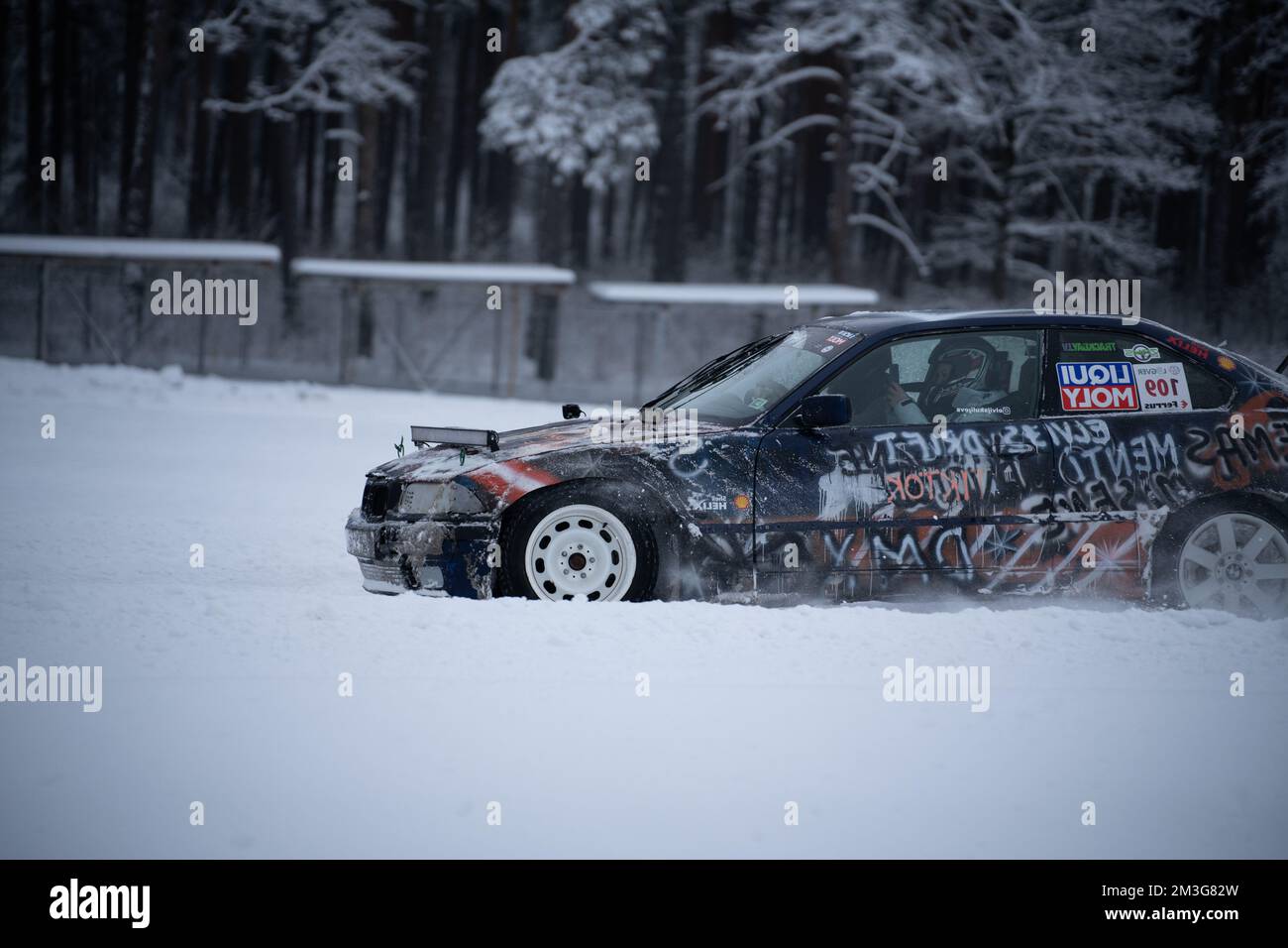12-12-2022 riga, Lettonia un'auto coperta di graffiti che guida attraverso la neve in un parcheggio con alberi sullo sfondo e una recinzione nel forgroun Foto Stock