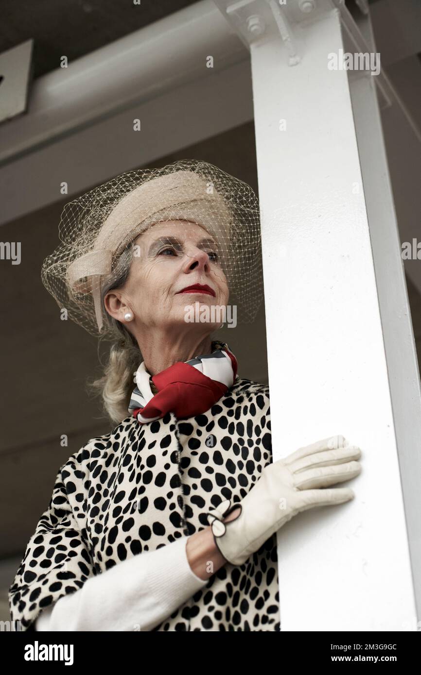 Donna alla moda che beve una gara , indossando un cappello con un velo al Goodwood Revival. Foto Stock