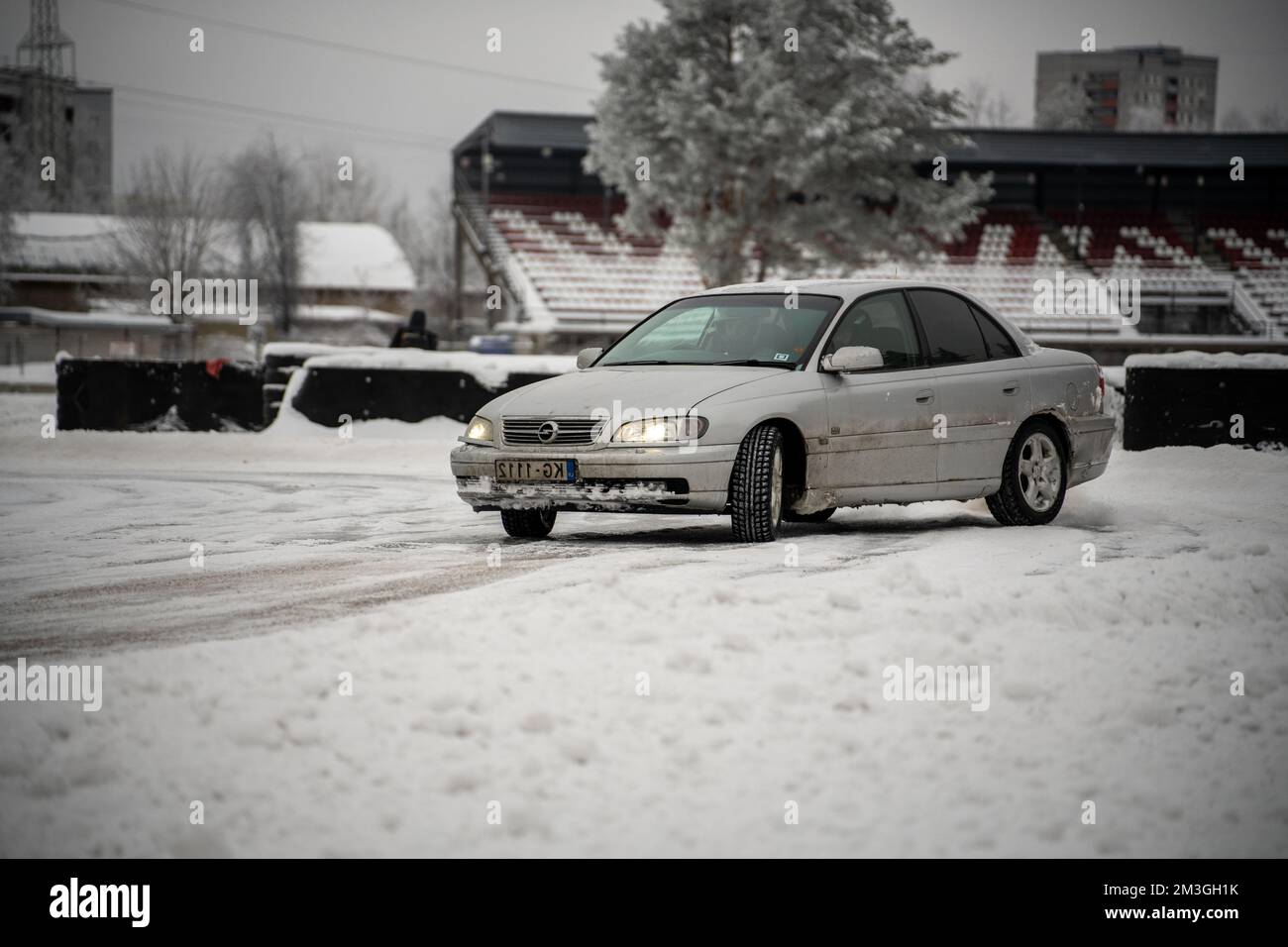 12-12-2022 riga, Lettonia un'auto parcheggiata su una strada innevata di fronte ad uno stadio con neve a terra e un edificio sullo sfondo. . Foto Stock