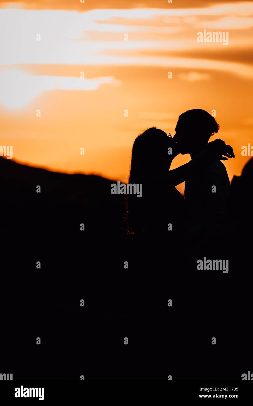 Un'immagine verticale di una bella silhouette di coppia baciata contro il vivace cielo del tramonto Foto Stock